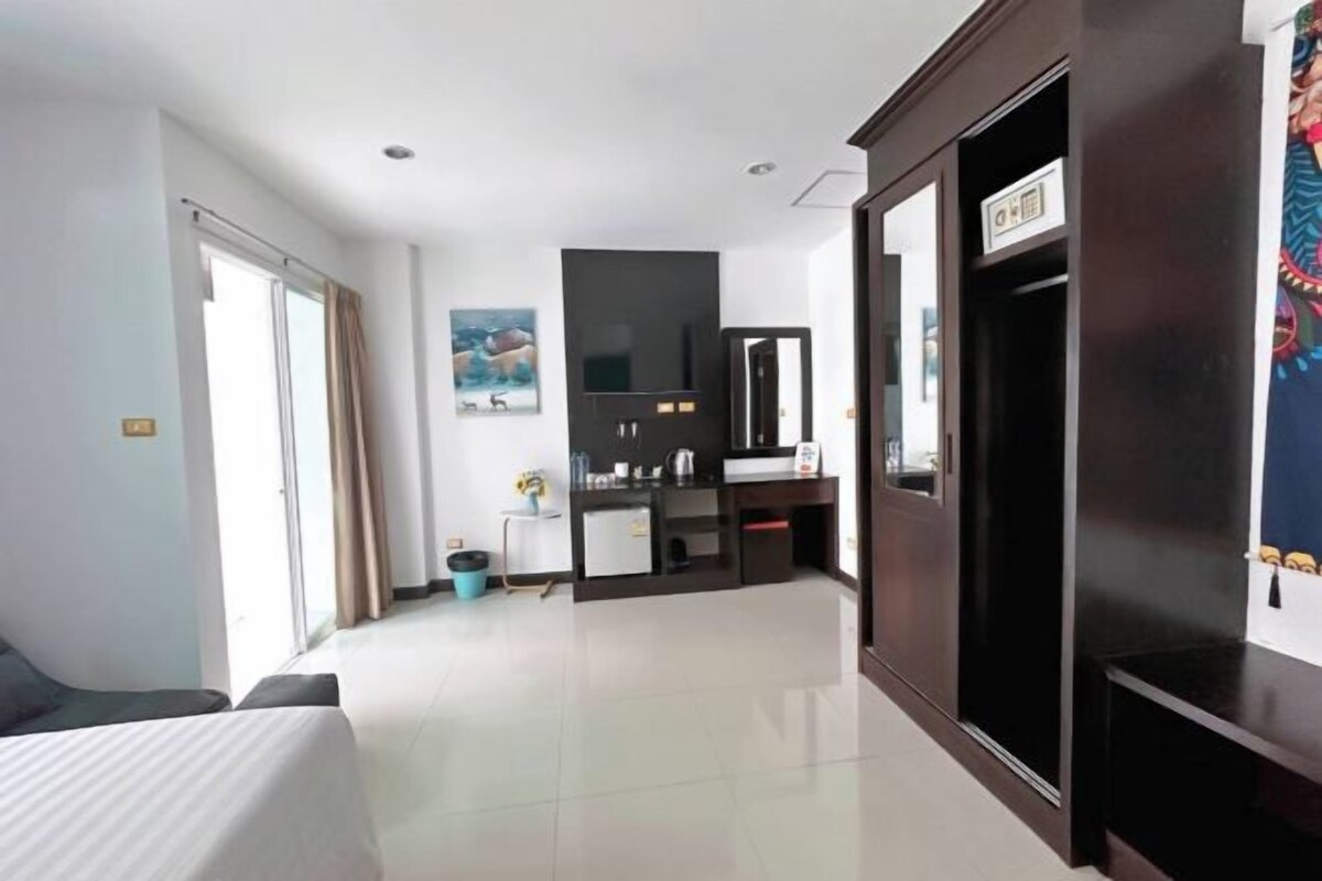 A hotel room with a bed, a small kitchenette, a television, and a large mirror.