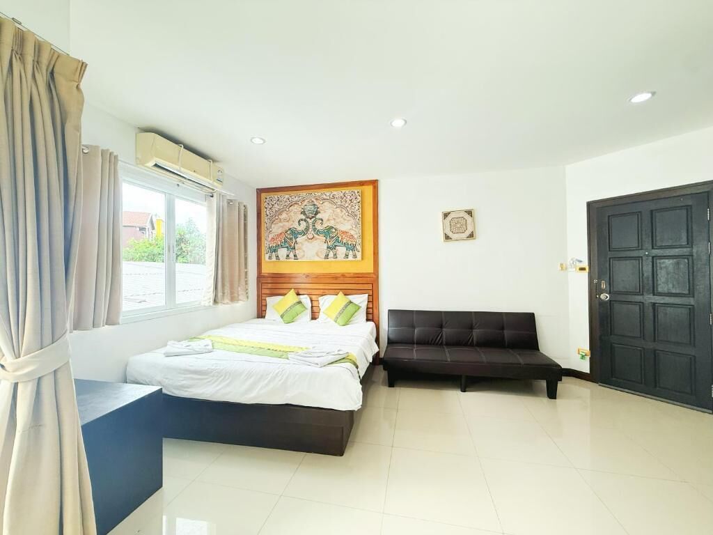 Habitación de hotel con cama, sofá negro, cabecera de madera, ventana con cortinas y una puerta.