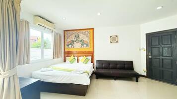 Habitación de hotel con cama, sofá negro, cabecera de madera, ventana con cortinas y una puerta.