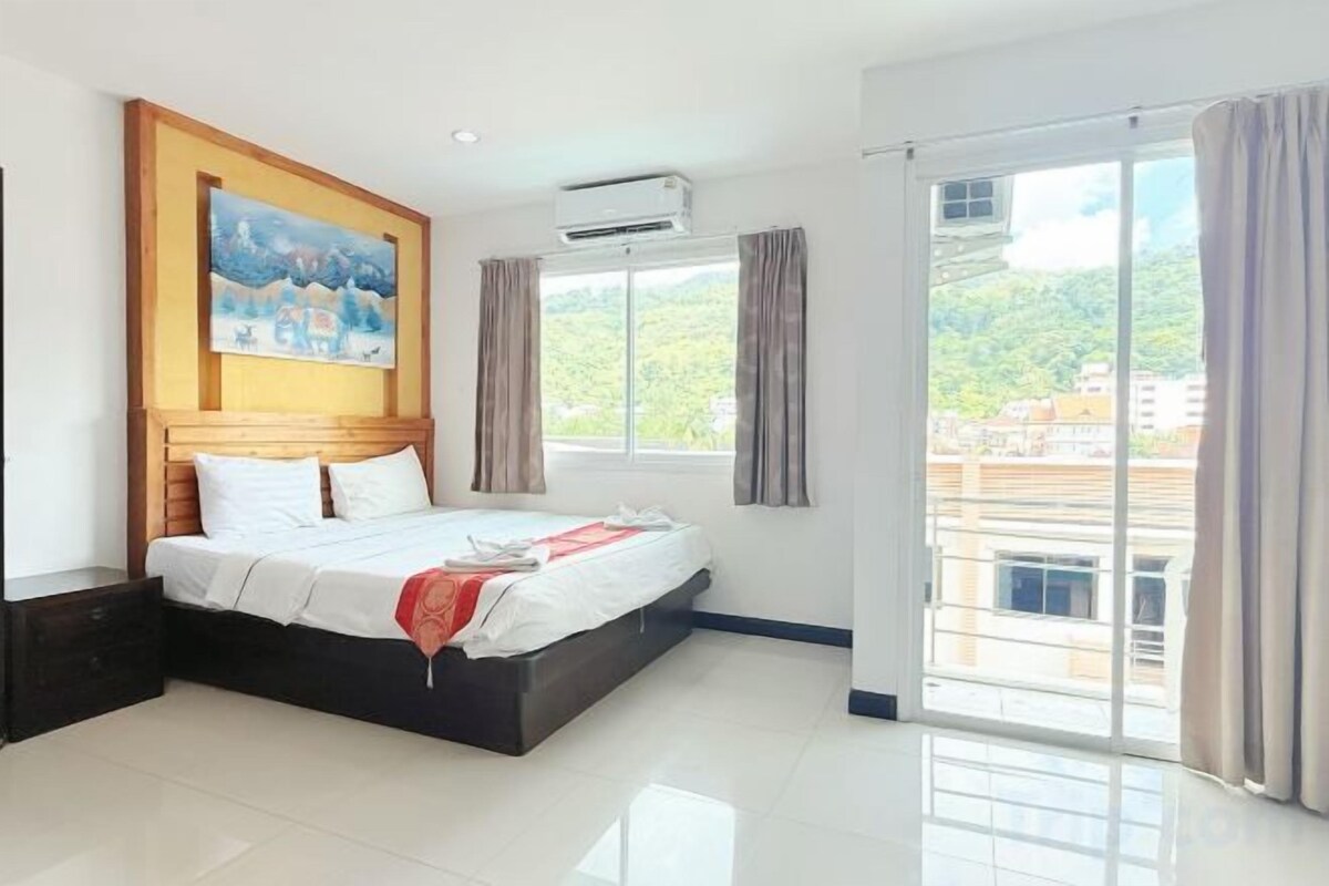 Une chambre d’hôtel avec un grand lit, un tableau au mur, un appareil de climatisation et une vue sur l’extérieur.