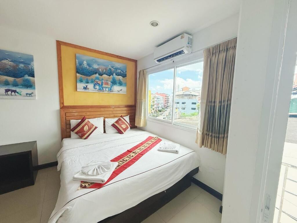 Hotelkamer met een bed, een raam met gordijnen, een wandairconditioner en twee ingelijste foto's.