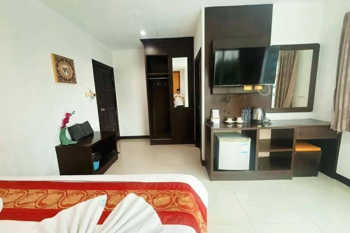 A hotel room with a bed, a desk, a TV, a mirror, and a wardrobe.