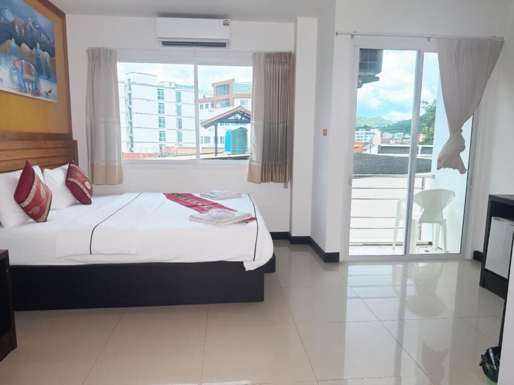 Habitación de hotel con cama, ventana con cortinas, vista de edificios y puerta que da a un balcón.