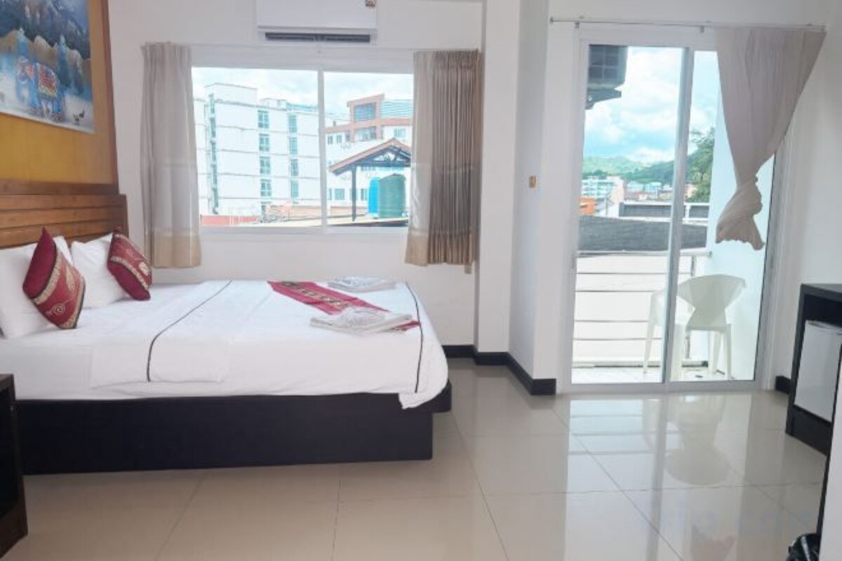 A hotel room with a bed, a window, and a view of buildings outside.