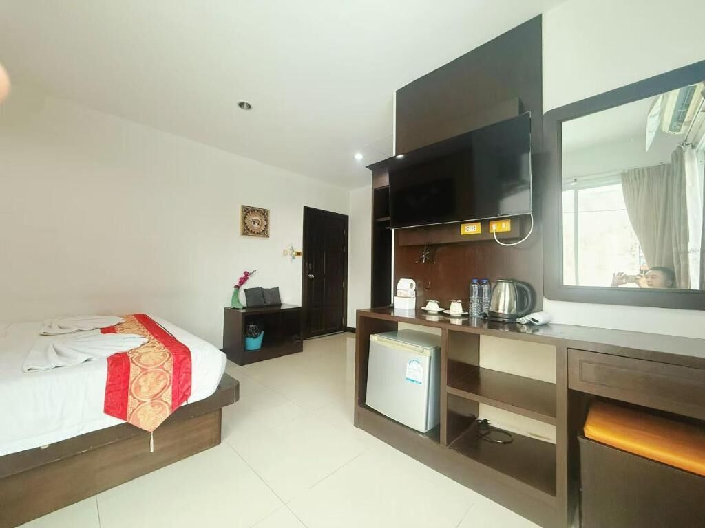 Een hotelkamer met een bed, bureau, kleine koelkast, spiegel en raam.