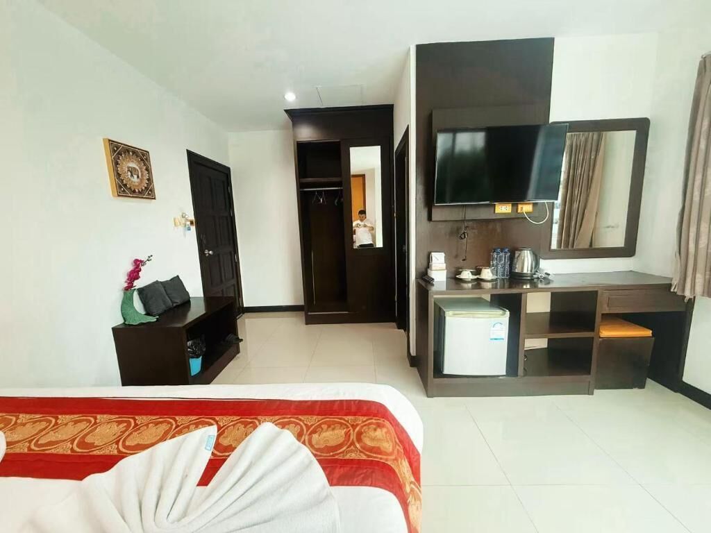 A hotel room with a bed, a desk, a television, a wardrobe, and a small refrigerator.