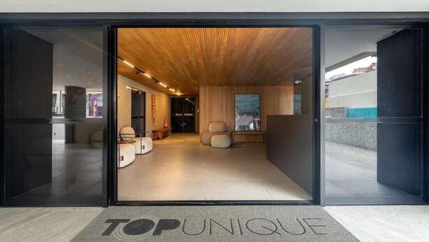 A modern interior with a wooden ceiling, a reception area with a sofa and chairs, and a 'TOP UNIQUE' sign on the floor. - Top Unique Maceió  (Maceió)