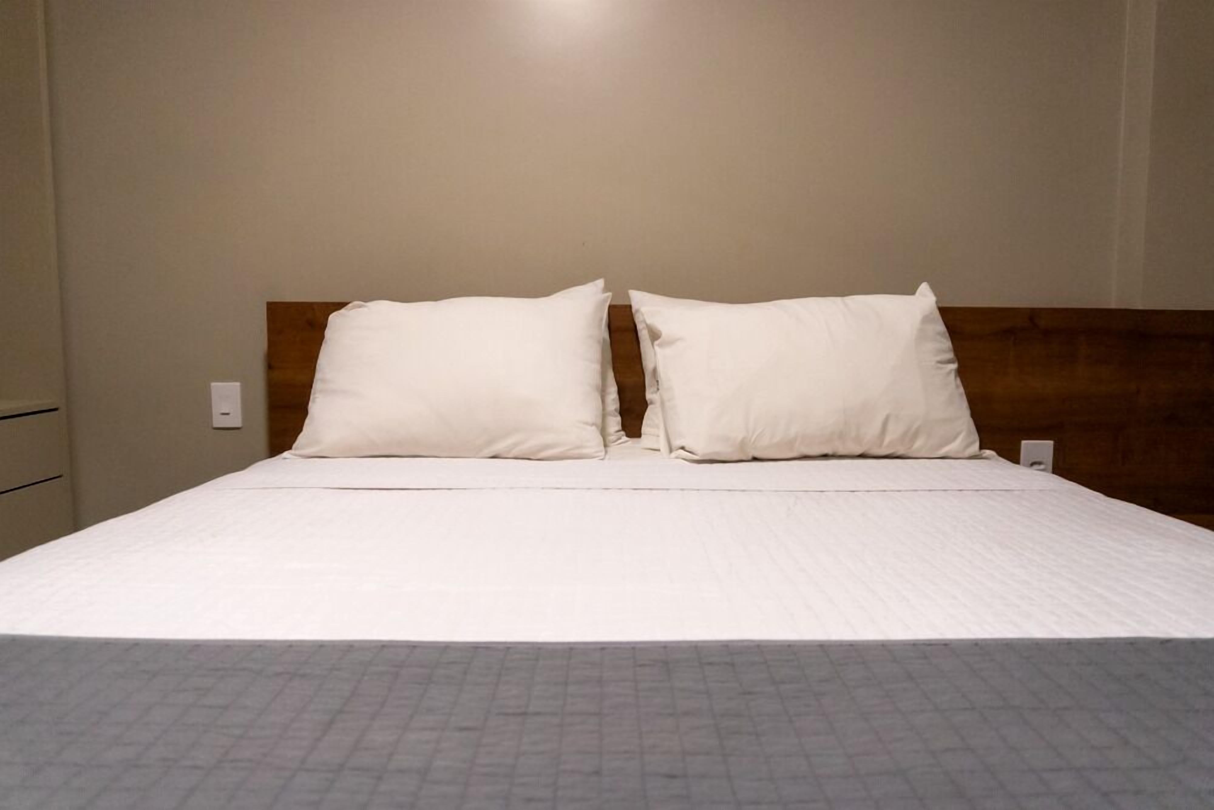 A bed with a wooden headboard, a white mattress, and a grey quilted bedspread.