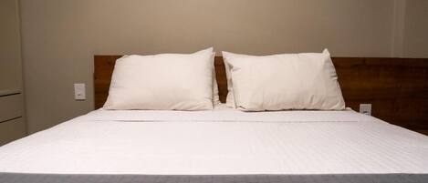 A bed with a wooden headboard, a white mattress, and a grey quilted bedspread.