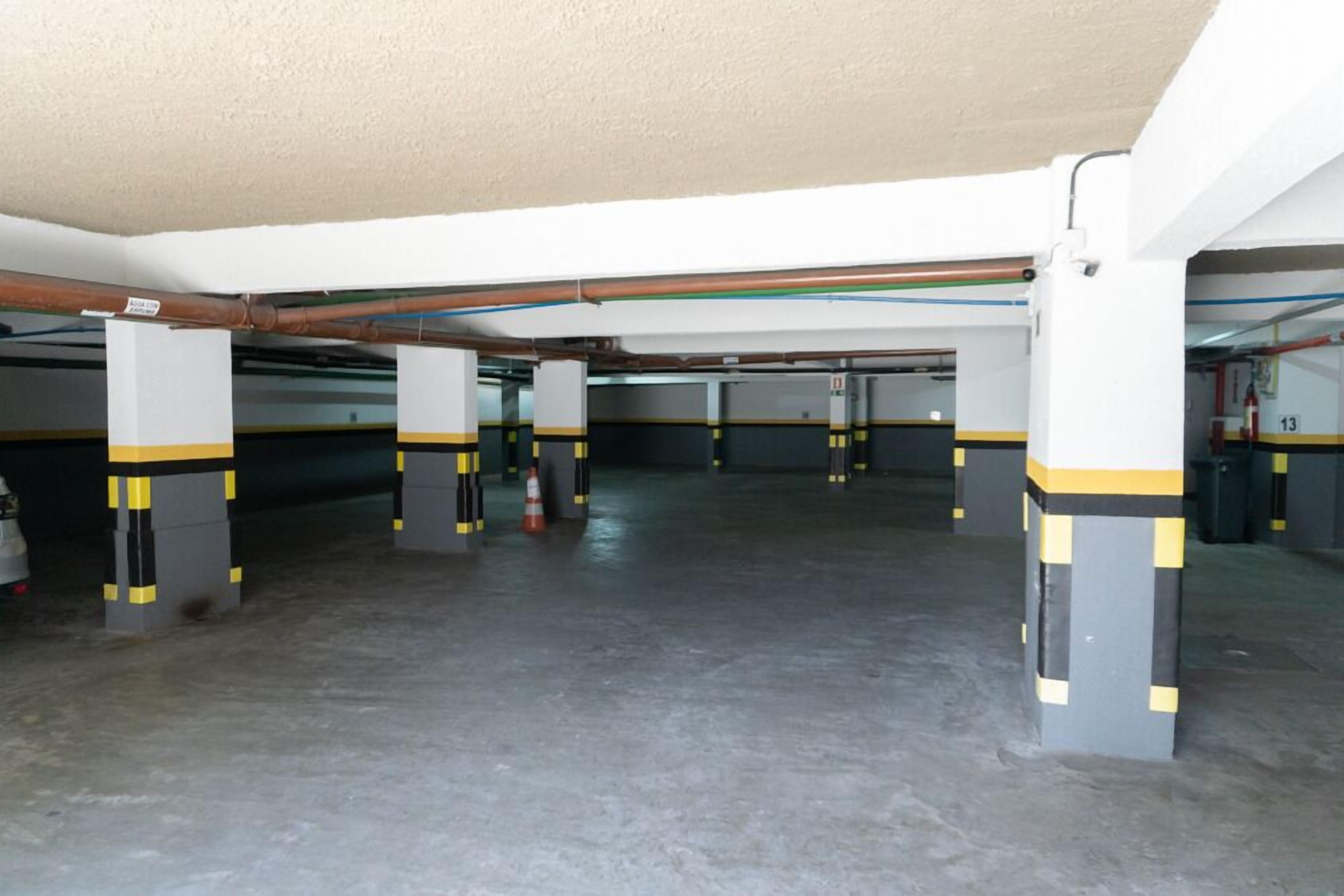 An indoor parking garage with concrete floors, yellow and black striped pillars, and visible pipes on the ceiling.