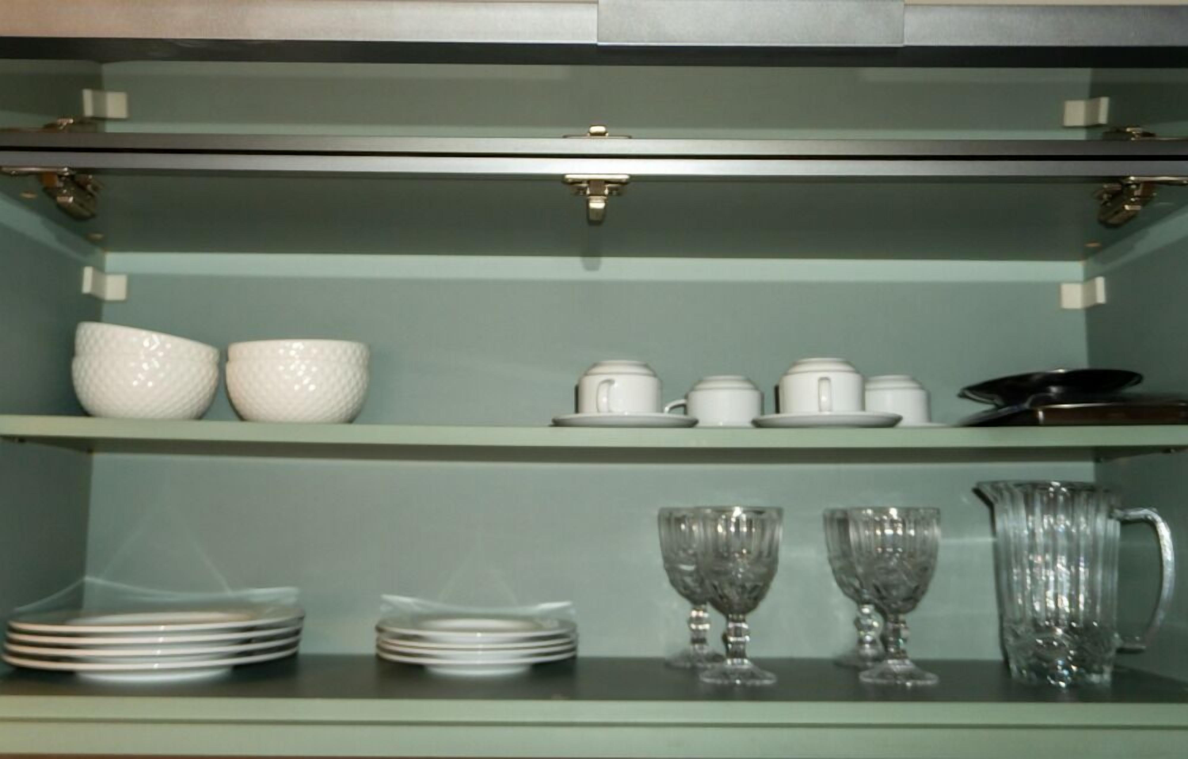 A kitchen with shelves holding white ceramic dishes, glassware, and a metal pitcher.
