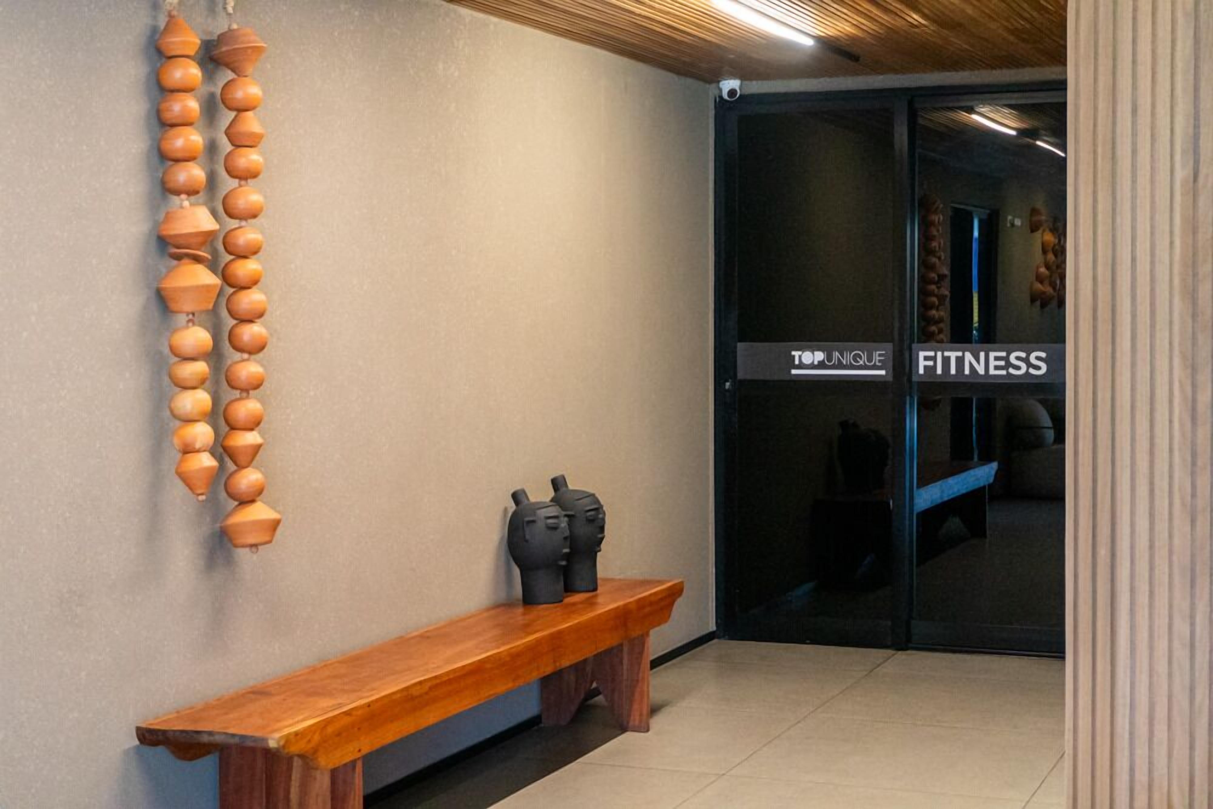 A hallway with a wooden bench, a wall-mounted decorative object, and a door labeled 'TOPUNIQUE FITNESS'.