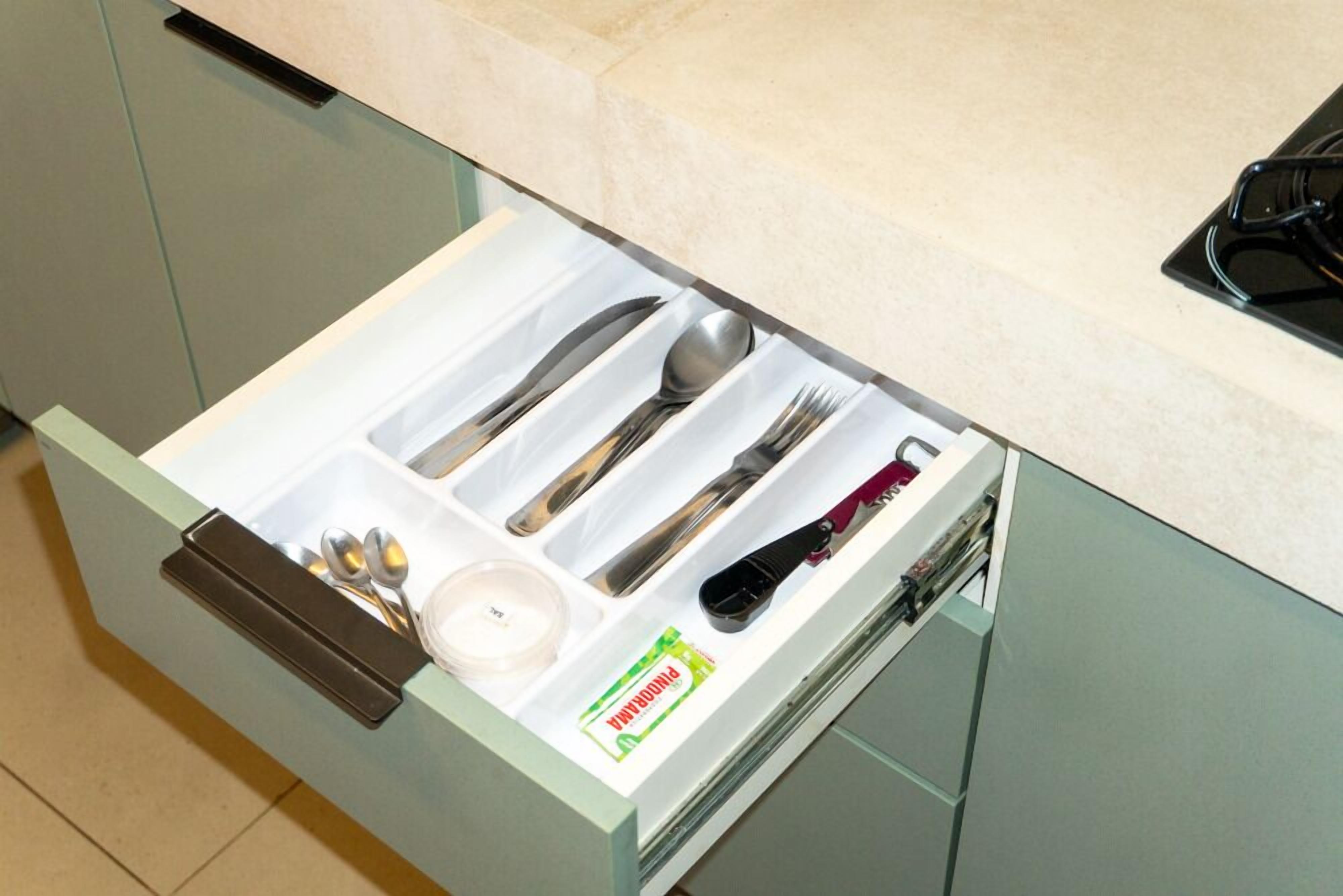 A kitchen drawer with utensils, a bottle, and a container.