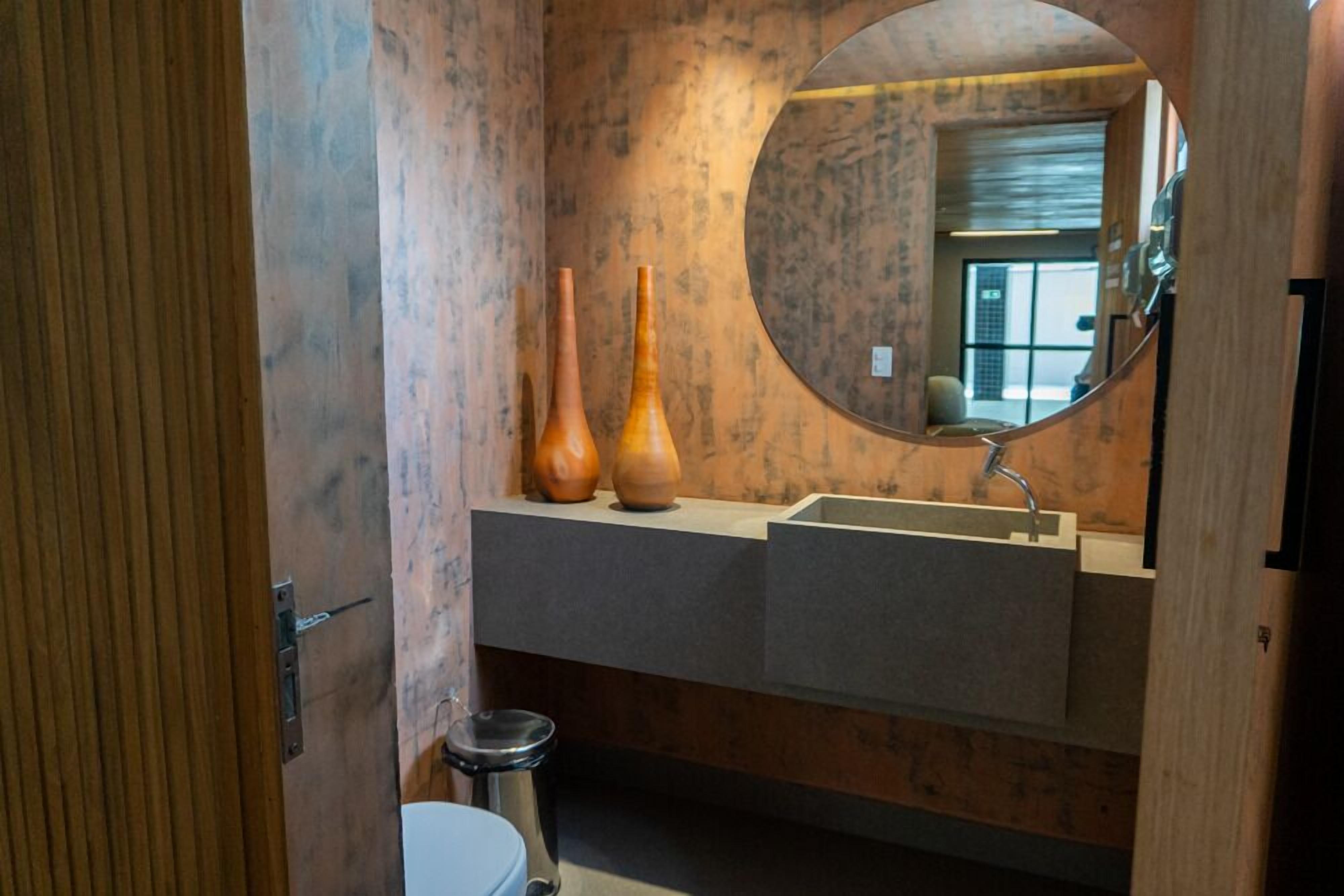 Un bagno con parete in legno, uno specchio rotondo, un lavandino e due vasi.