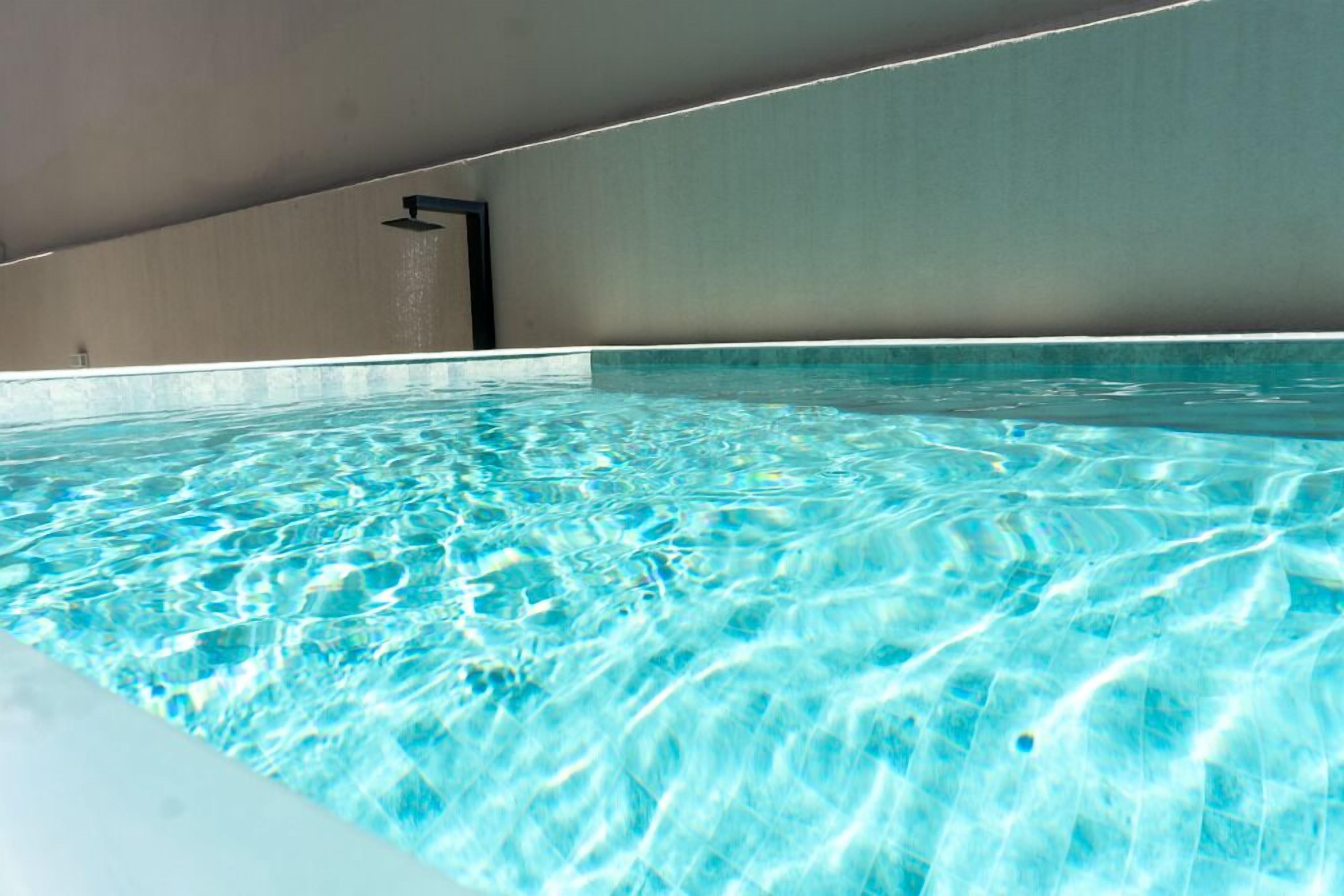 An indoor swimming pool with clear water, a sloped ceiling, and a wall-mounted faucet.