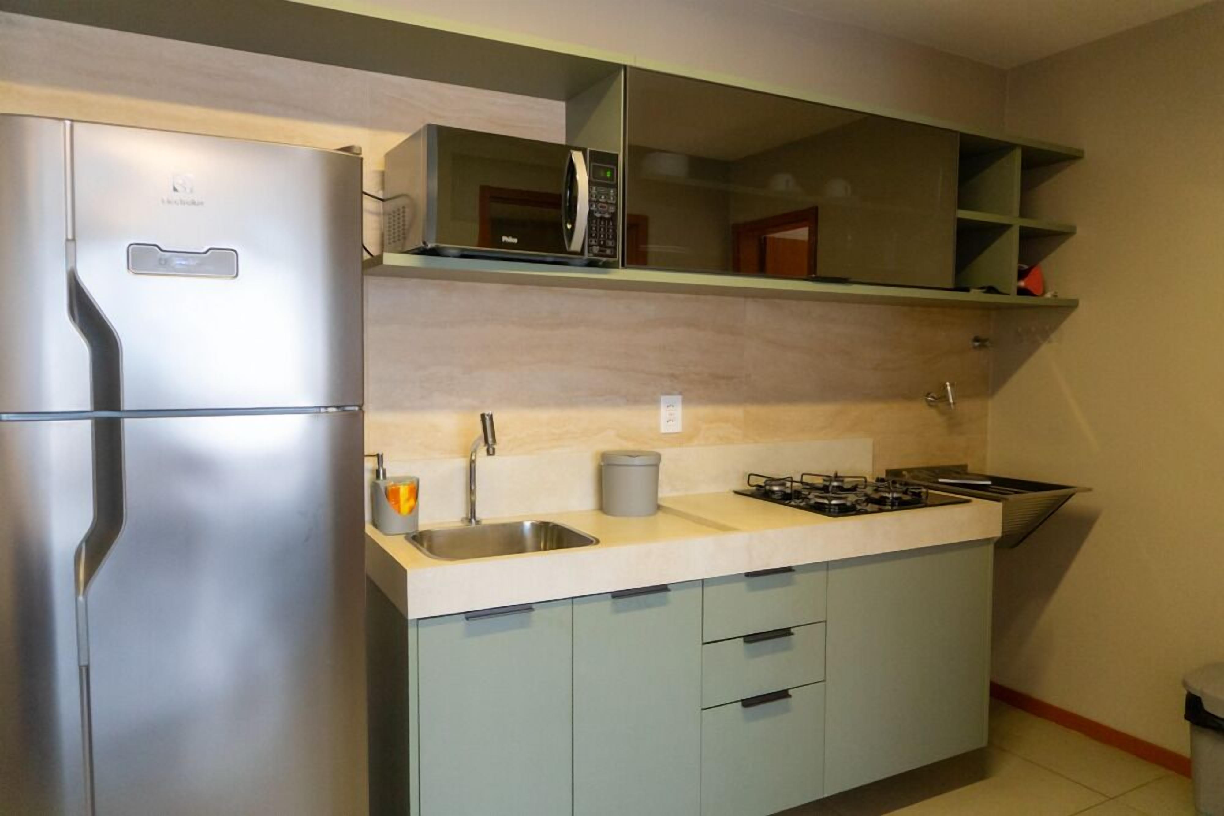 Una cocina compacta con refrigerador de acero inoxidable, microondas, estufa a gas y armarios de color claro.