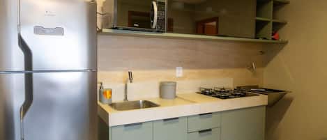 Una cocina compacta con refrigerador de acero inoxidable, microondas, estufa a gas y armarios de color claro.