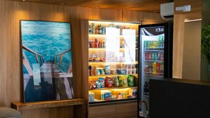 A room with a wooden wall, a large framed picture of a sea view, a refrigerator stocked with beverages, and a wooden bench. - Top Unique Maceió  (Maceió)