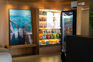 Una habitación con pared de madera, un cuadro grande enmarco con vista al mar, un refrigerador lleno de bebidas y un banco de madera.