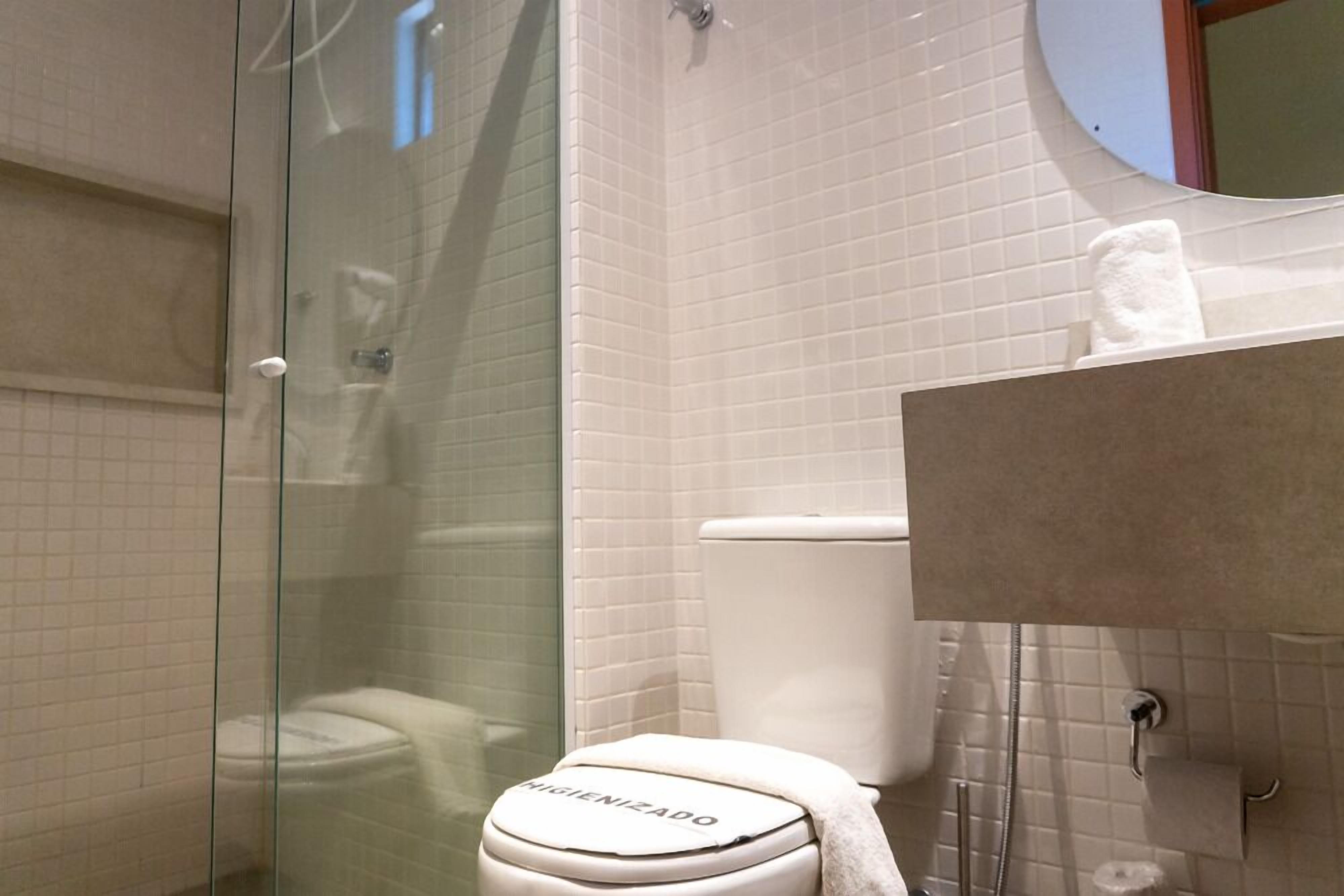 A bathroom with a glass shower enclosure, a toilet with a towel on it, and a mirror above the sink.