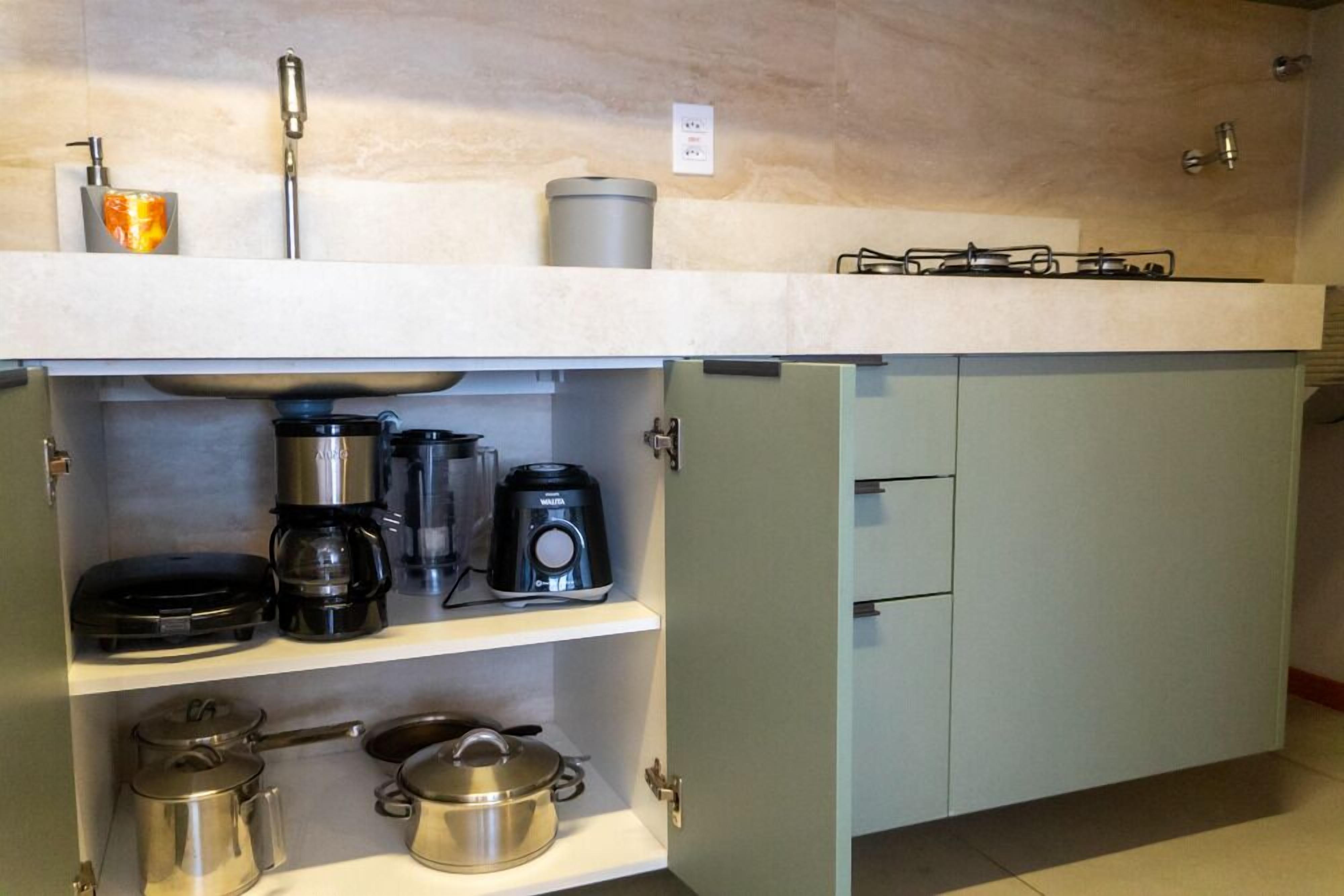 Een keuken met een fornuis, koffiezetapparaat, pannen en een magnetron.