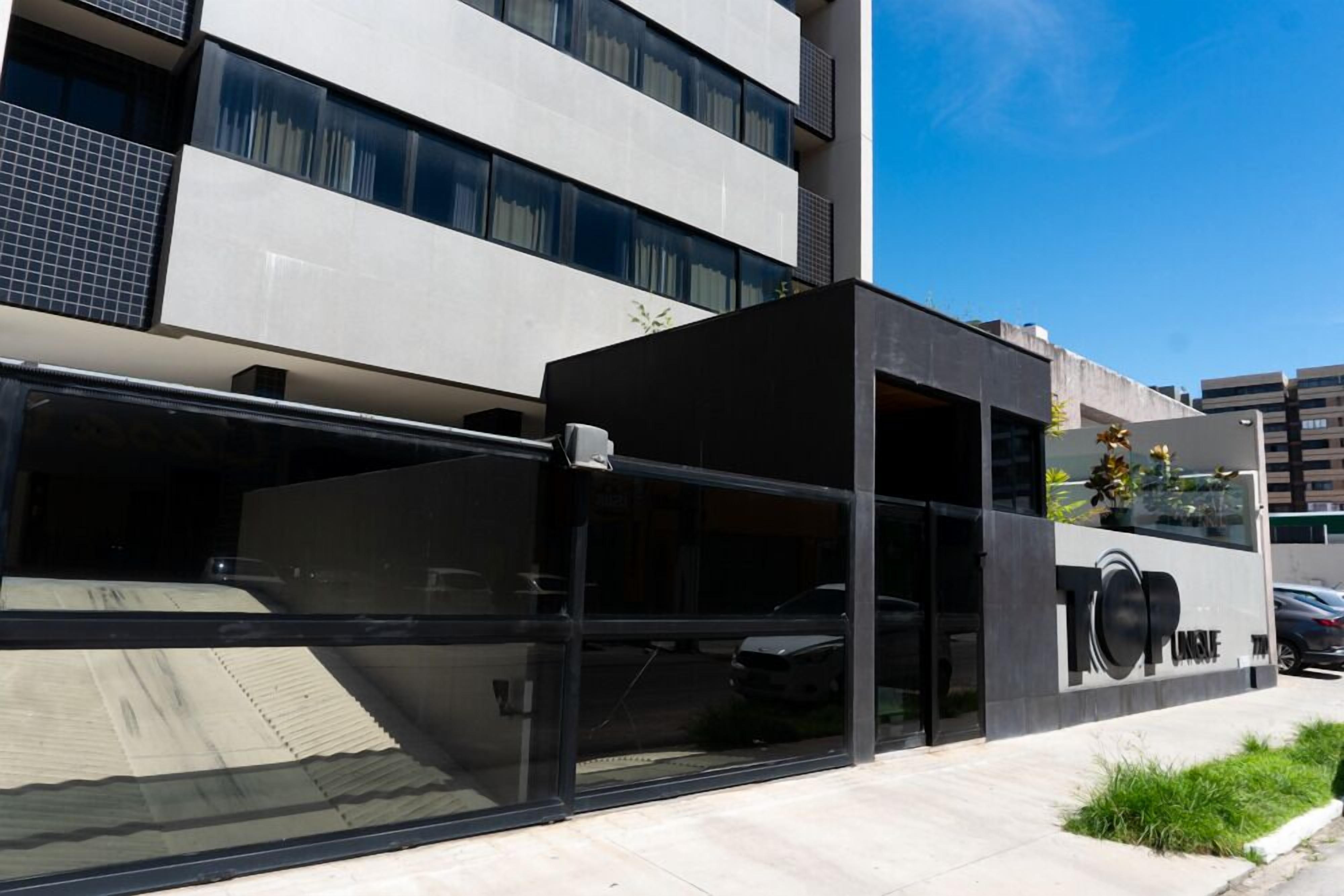 Un edificio moderno con fachada de vidrio, un acceso cubierto y un coche estacionado afuera.