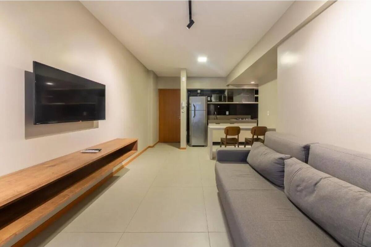 A modern living room with a flat-screen TV mounted on the wall, a wooden bench, and a grey sofa.