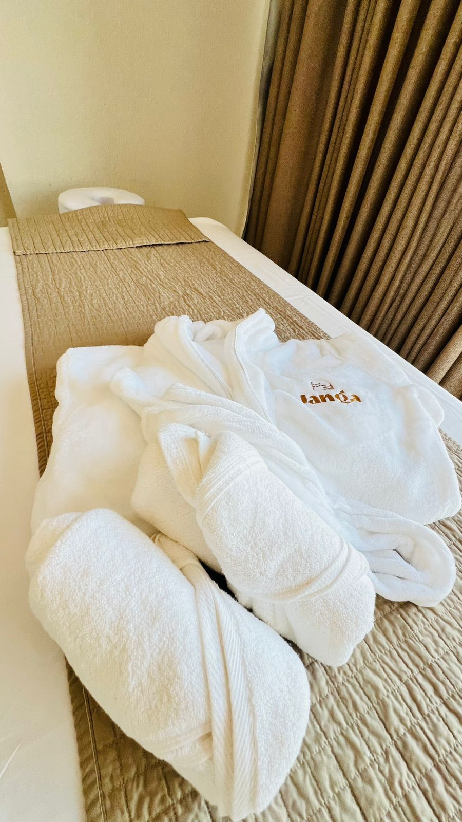 A neatly made bed with a beige quilt and a white pillow.