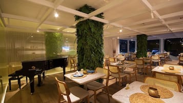 A restaurant with a piano, tables with woven placemats, and large green vertical gardens.