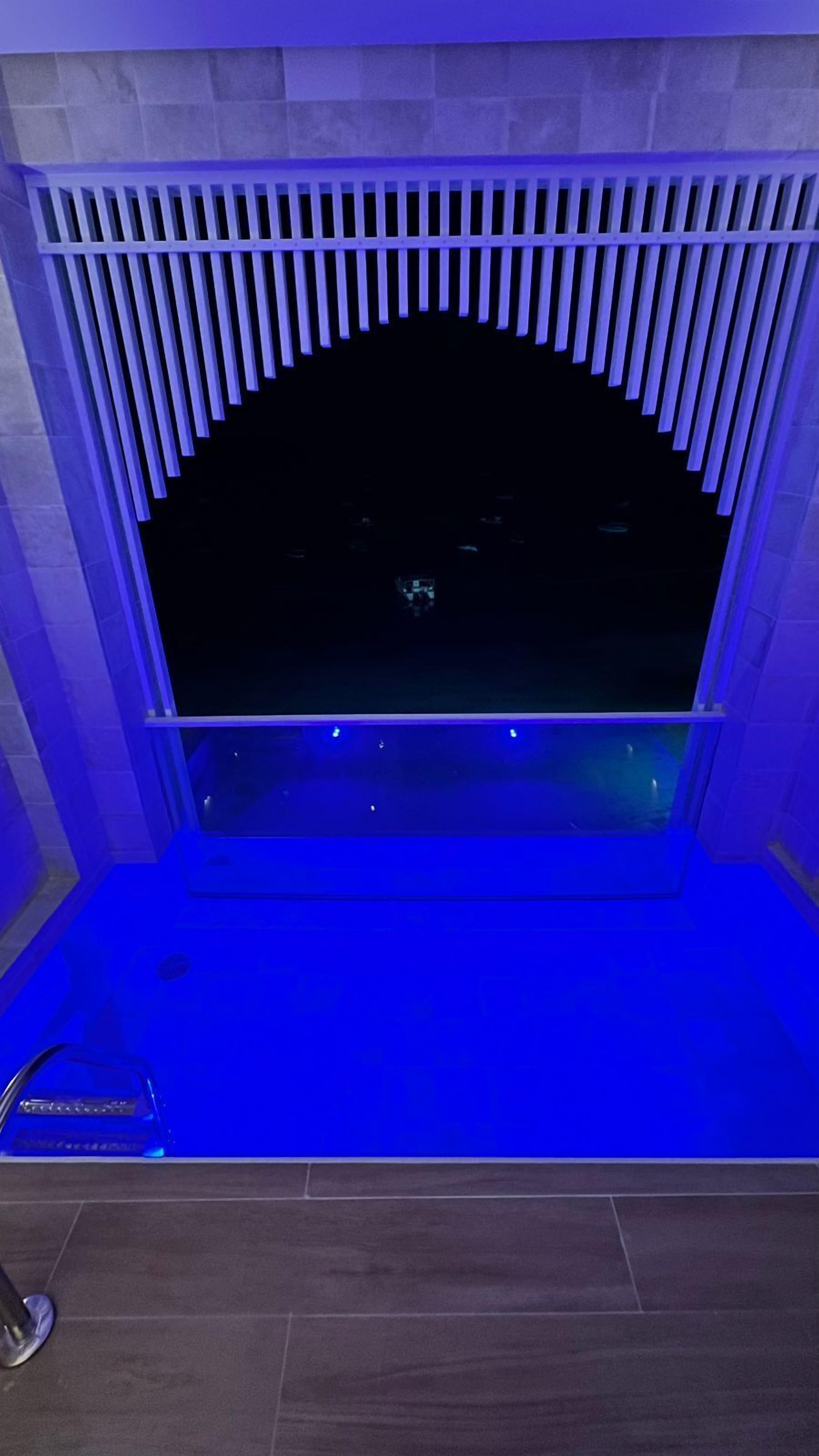 A room with a large darkened window, a blue-lit seating area, and a tiled floor.