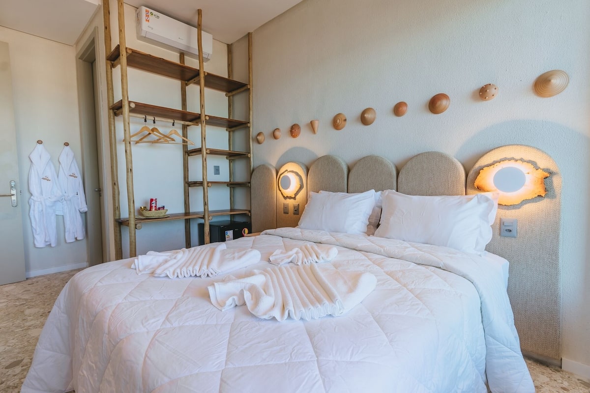 Un lit bien fait, recouvert d’une courtepointe, une échelle en bois et une étagère fixée au mur, sur laquelle sont posées des serviettes et un panier.
