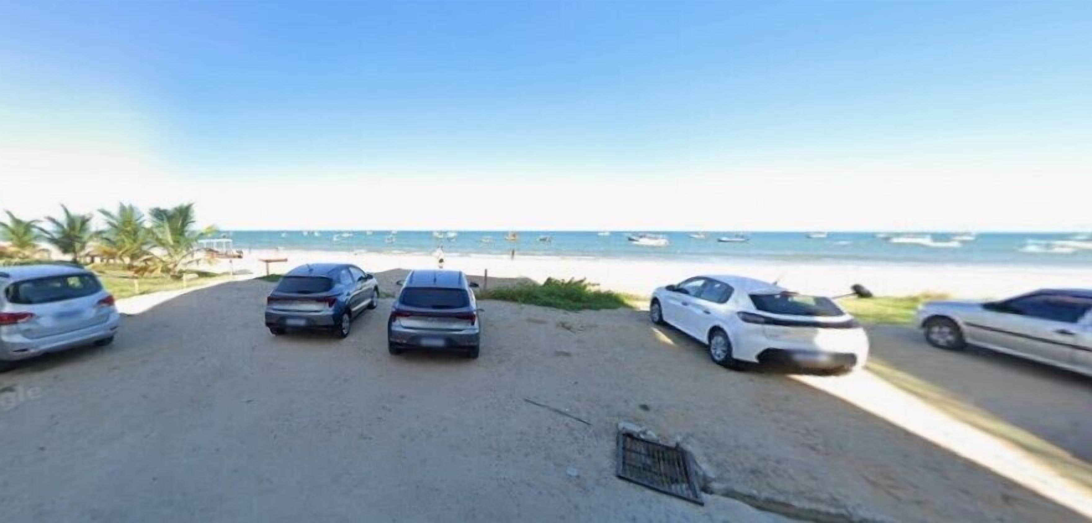A parking area with several cars and a beach in the background.