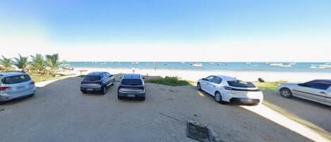 A parking area with several cars and a beach in the background.
