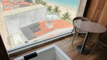 Un baño moderno con una bañera grande, vistas a una playa y una pequeña mesa con sillas.