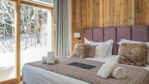 A bedroom with a wooden headboard, a large bed with white linens, and a view of a snowy outdoor area through a glass door. - Outstanding 5 Bedroom Luxury Chalet, close to village centre, hot tub and sauna (Les Gets)