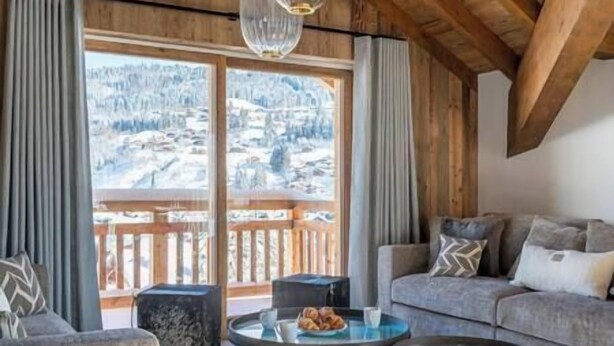 A cozy room with a wooden ceiling, a grey sofa, a round glass table with pastries, and a view of a snowy landscape through large windows. - Outstanding 5 Bedroom Luxury Chalet, close to village centre, hot tub and sauna (Les Gets)