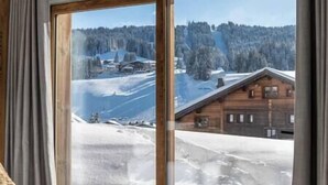 A room with a large window overlooking a snowy landscape with a wooden cabin. - Outstanding 5 Bedroom Luxury Chalet, close to village centre, hot tub and sauna (Les Gets)