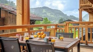 Une terrasse en bois avec une table dressée pour le petit-déjeuner, offrant une vue sur un paysage montagneux.