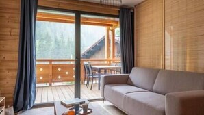 Un salon chaleureux avec un canapé, une table à manger et des chaises, et une vue sur une terrasse en bois et un bâtiment situé à l’extérieur.