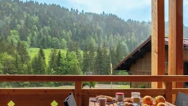Une terrasse en bois avec une table dressée pour le petit-déjeuner, offrant une vue sur une montagne boisée.