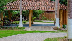 Un kiosque doté d’un toit en tuiles, entouré de palmiers et bordé d’un chemin de gravier.
