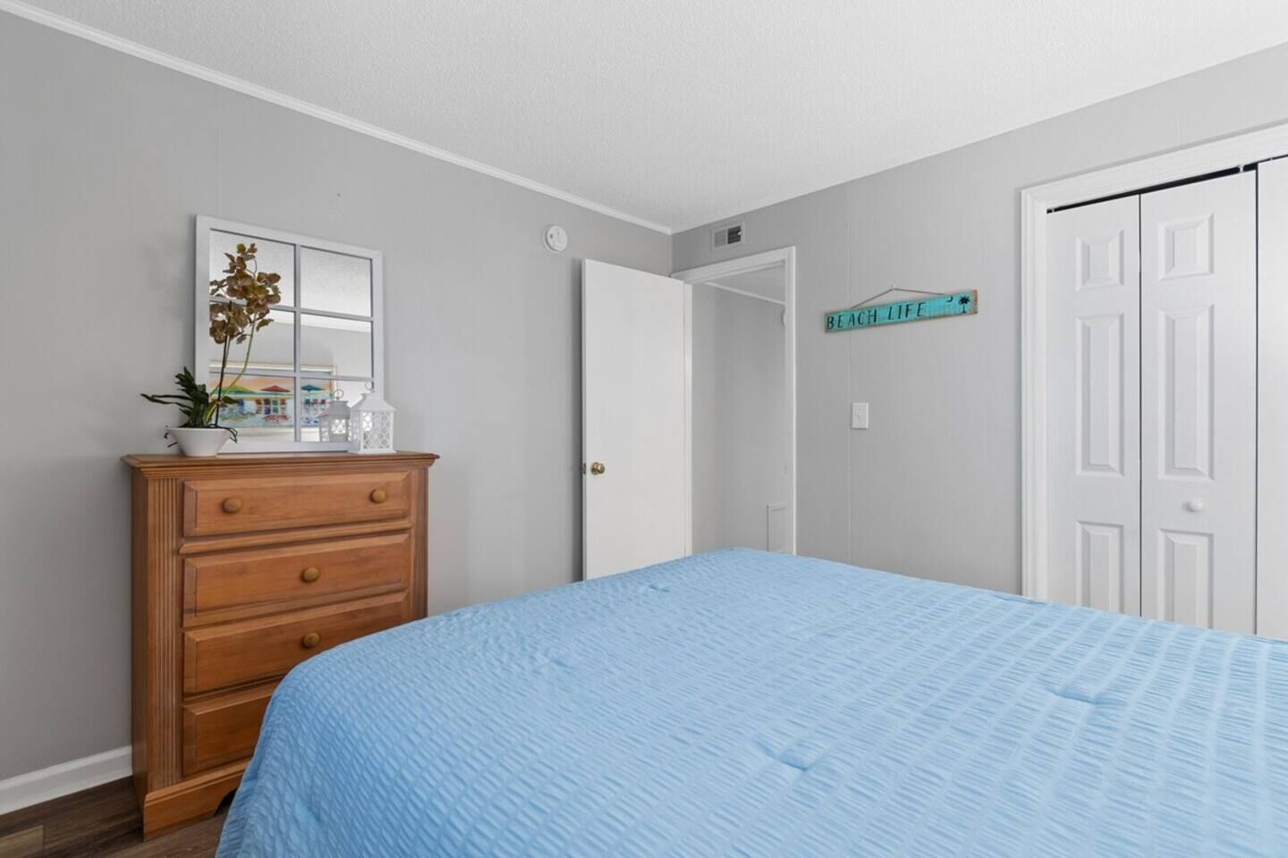 Une chambre à coucher avec un lit, une commode, un miroir, une porte et un panneau accroché au mur.