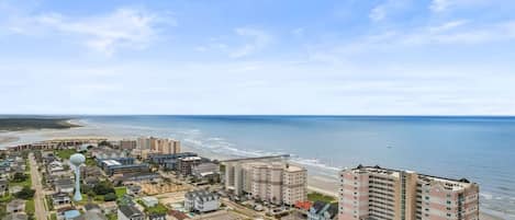 A coastal cityscape with a beachfront hotel, residential buildings, and a clear view of the ocean.