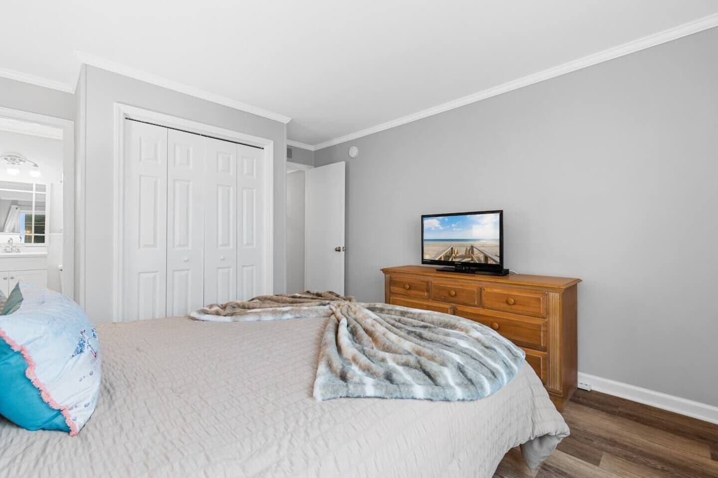 Een slaapkamer met een bed, een houten dressoir, een televisie en een deur.