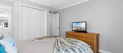 Een slaapkamer met een bed, een houten dressoir, een televisie en een deur.