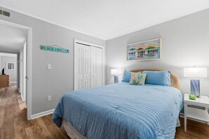 A bedroom with a large bed, a nightstand, a lamp, a painting, and a sign on the wall. - Beachside Hideout- Pool- 3 Bds- Elevator (North Myrtle Beach)
