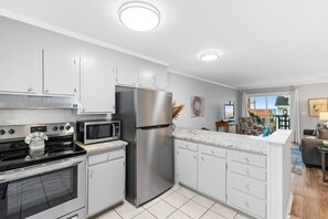 A modern kitchen with stainless steel appliances, white cabinetry, and a view to the living area. - Beachside Hideout- Pool- 3 Bds- Elevator (North Myrtle Beach)