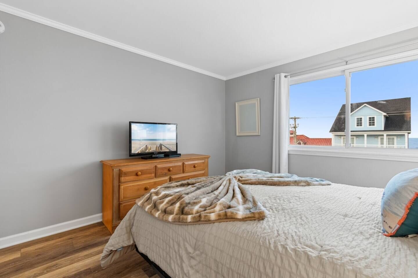 Une chambre à coucher comprenant un lit, une commode, un téléviseur et une fenêtre donnant sur une maison.