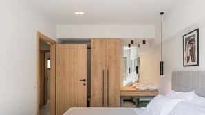 A modern bedroom with a bed, wooden wardrobe, a bedside table with towels, a mirror, and a hanging light fixture.
