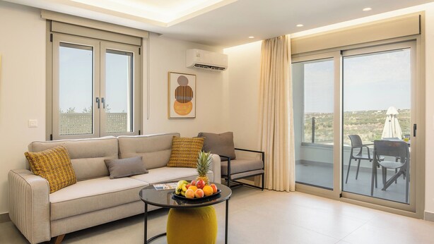 A modern living room with a sofa, a coffee table with fruit, and a balcony with chairs.